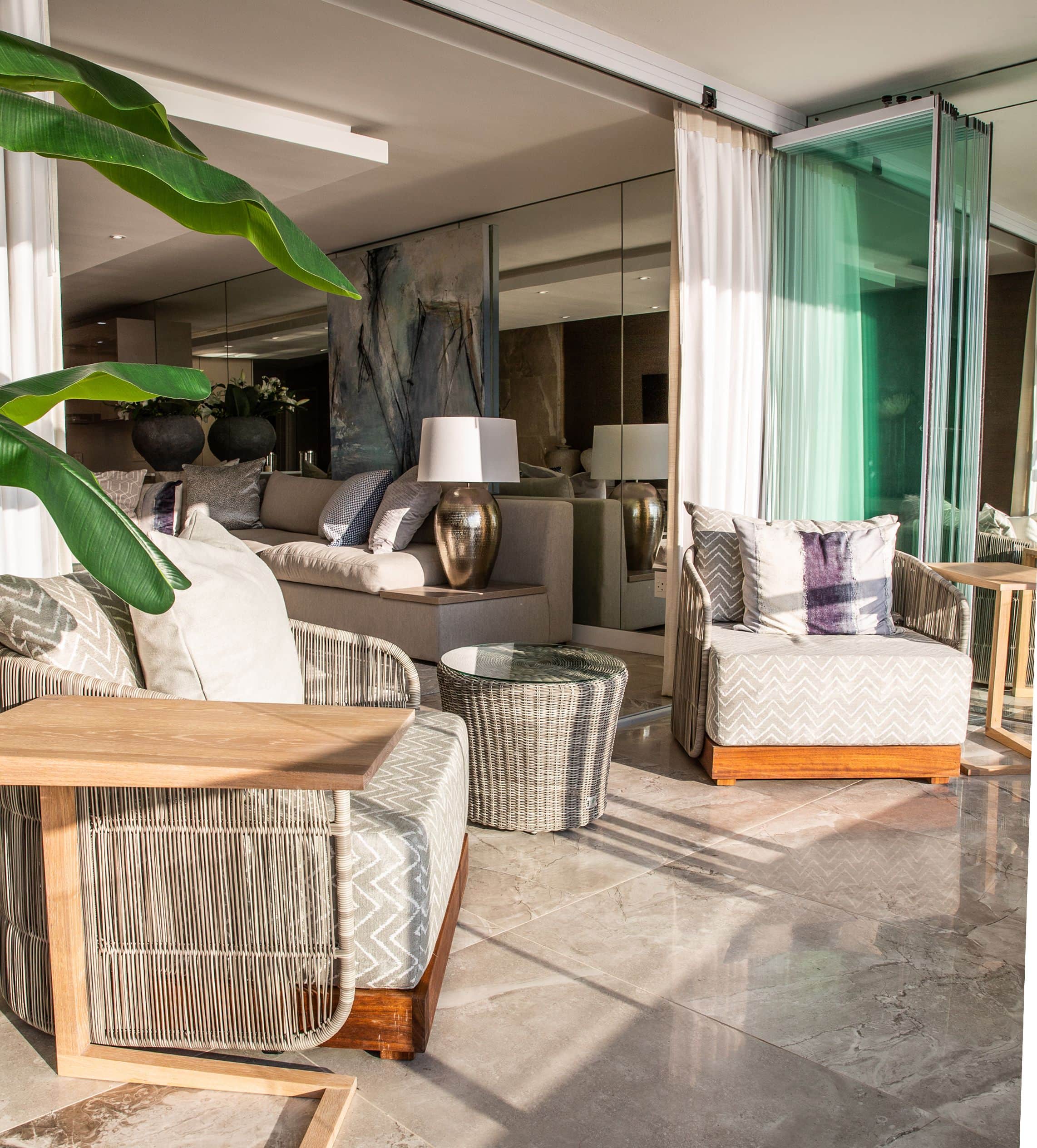 Terrace with woven armchairs and side tables on marble flooring, glass doors folded back to the lounge
