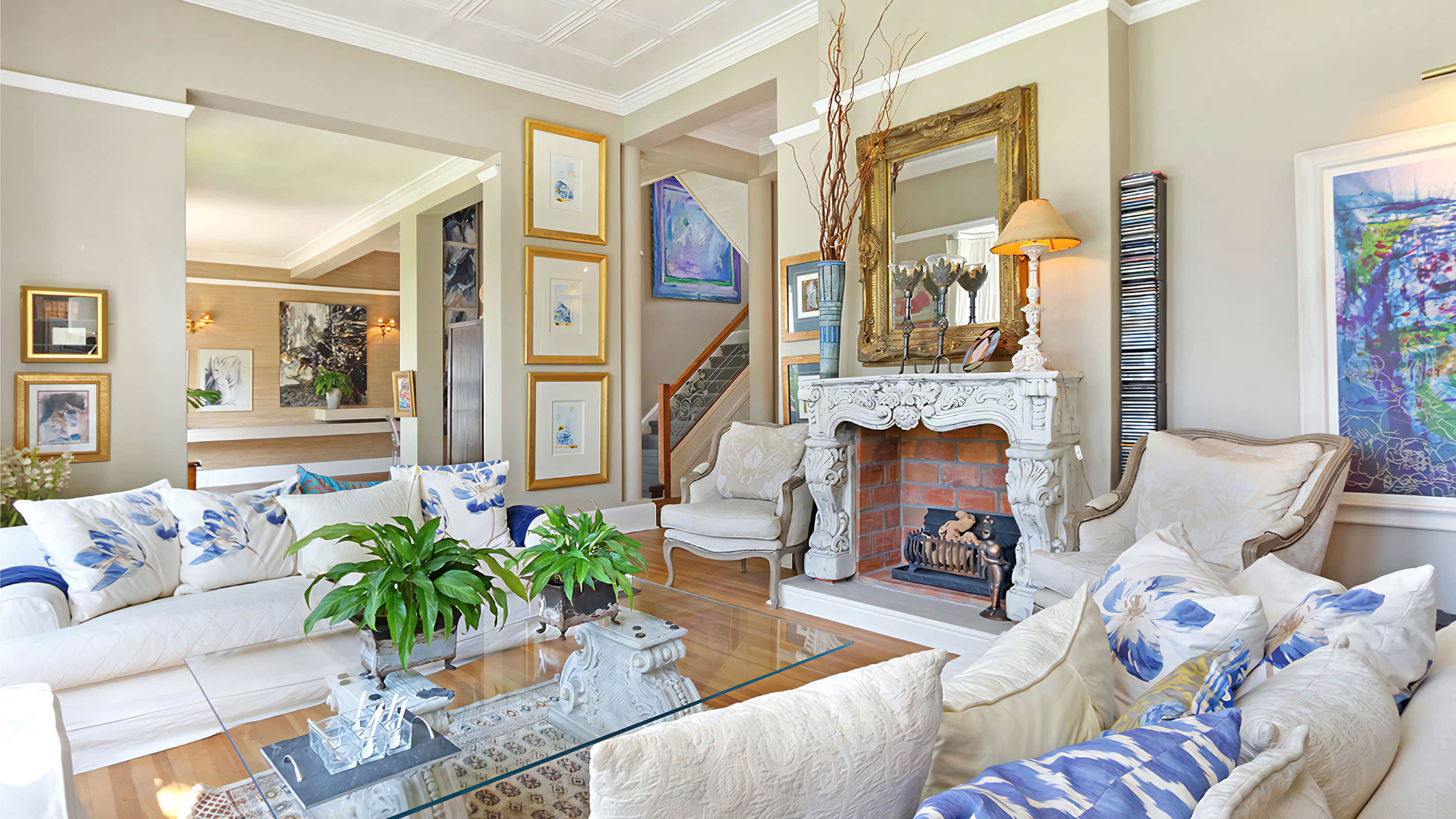 Living room with white slipcovered sofas, blue and white cushions, a carved marble fireplace and a gilt mirror
