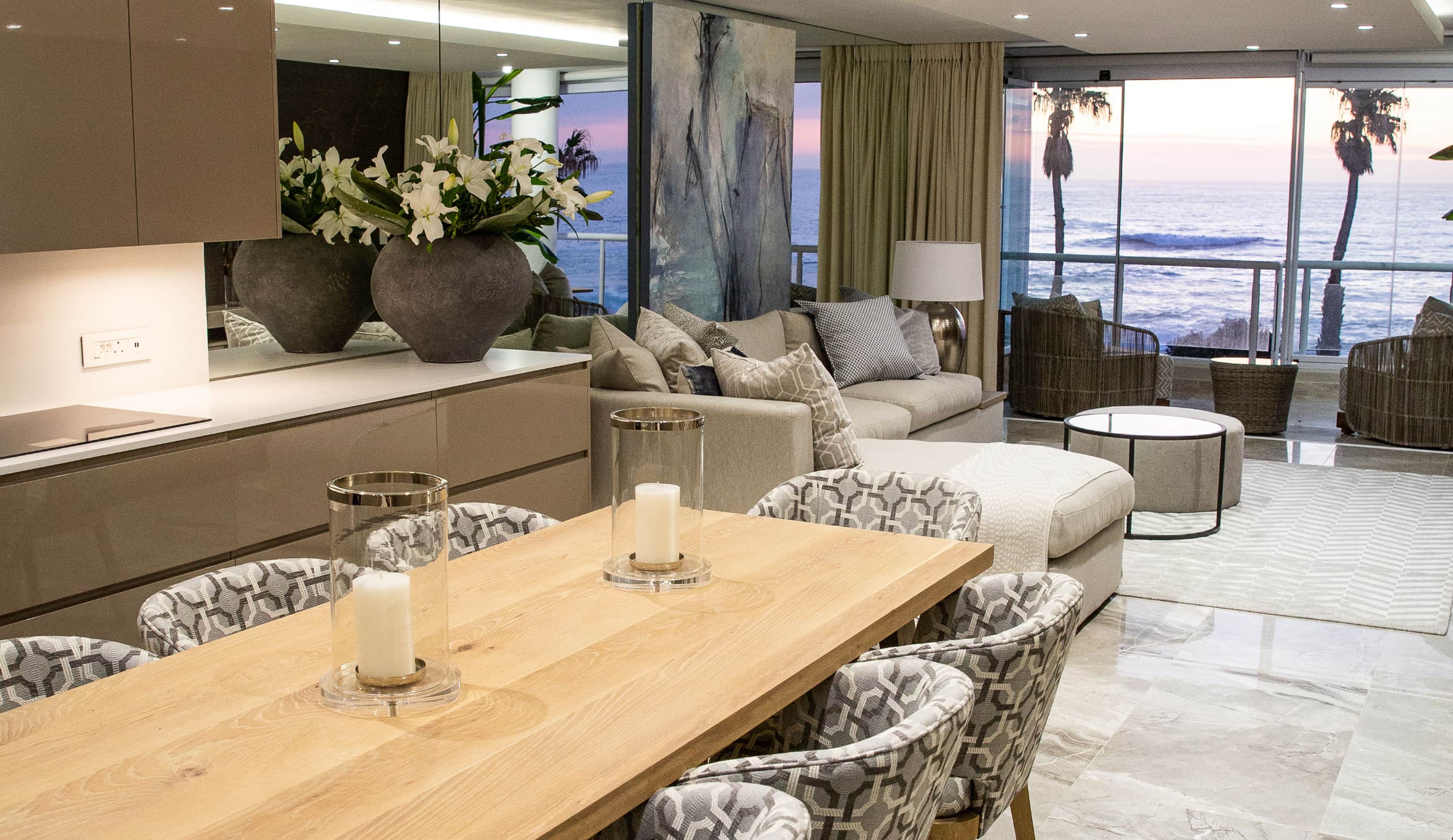 Oak dining table with patterned chairs and candles, open to a lounge with an ocean view
