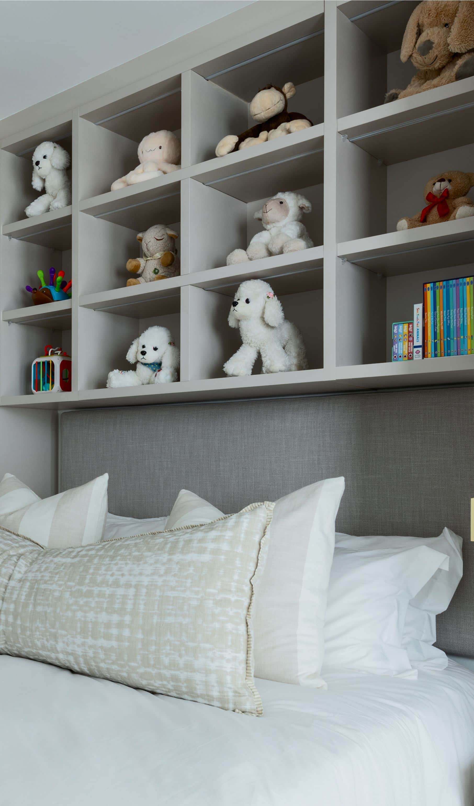 Child’s bed beneath built-in shelves of soft toys and books, with a grey upholstered headboard