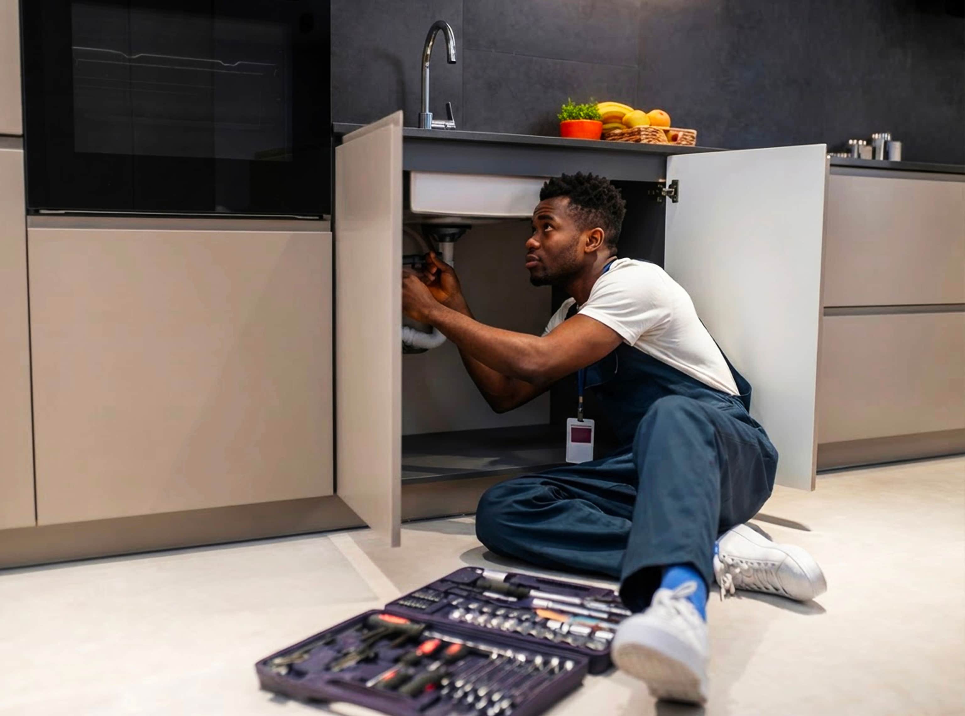 Installer fitting plumbing under a kitchen sink, with a tool case open on the floor