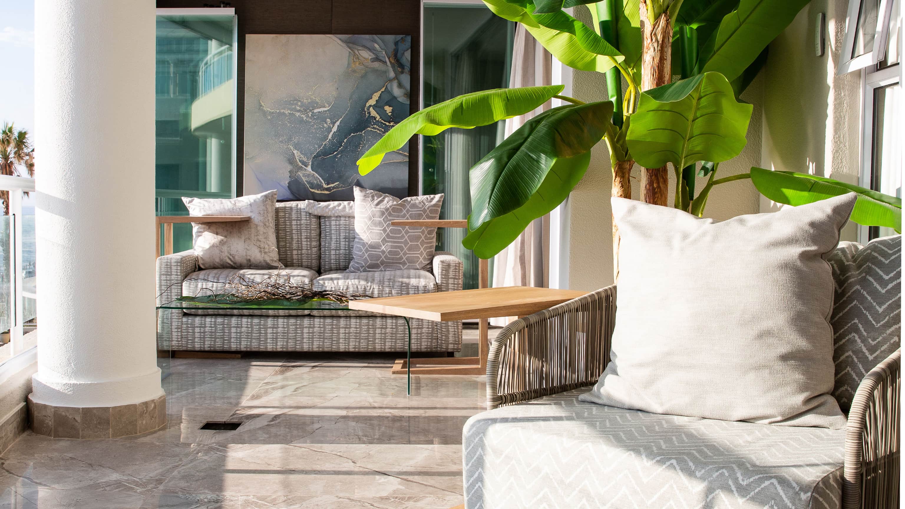 Terrace with woven armchairs, a banana plant and marble flooring, looking out to sea