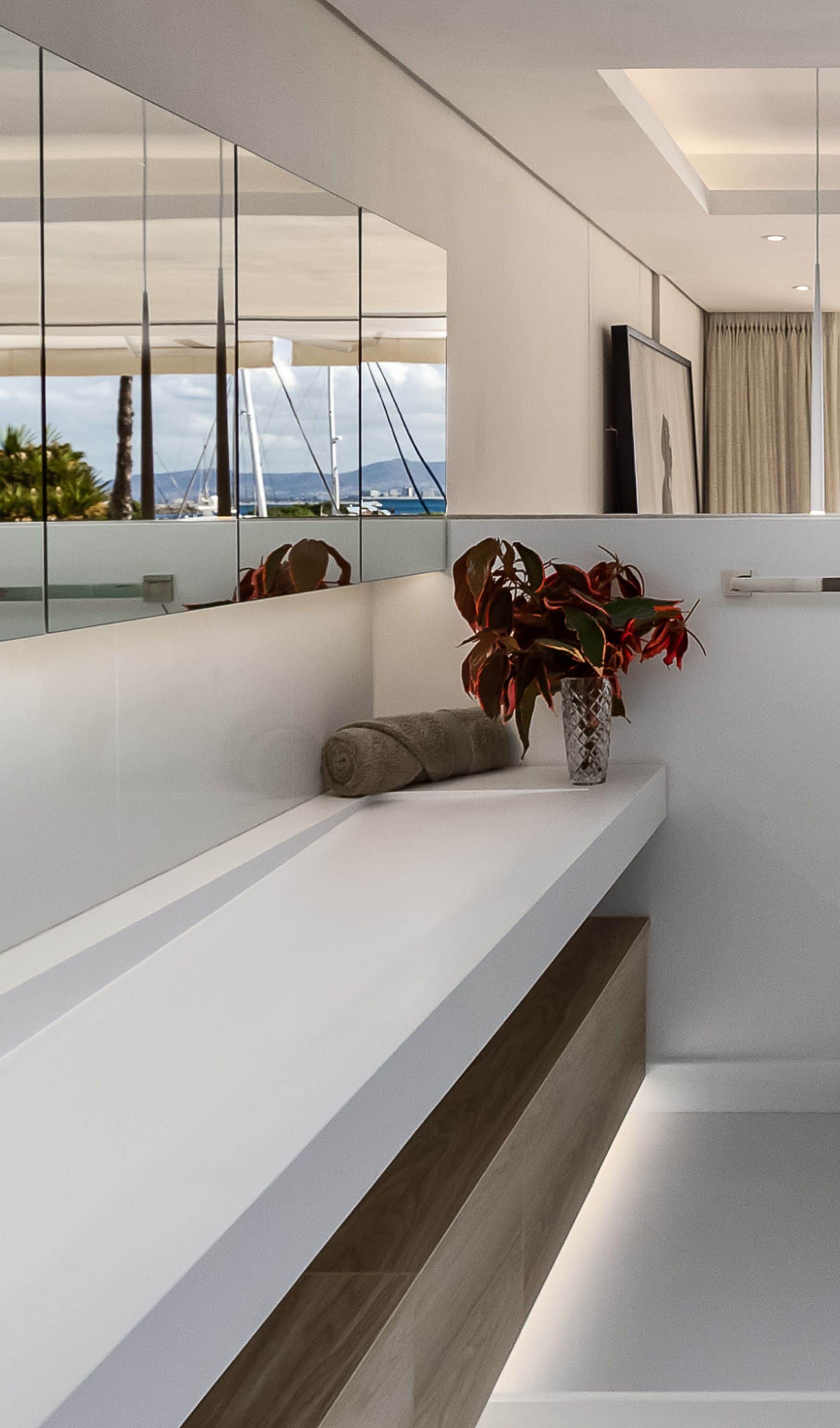 Long white basin on oak cabinetry, with a mirrored wall reflecting the marina