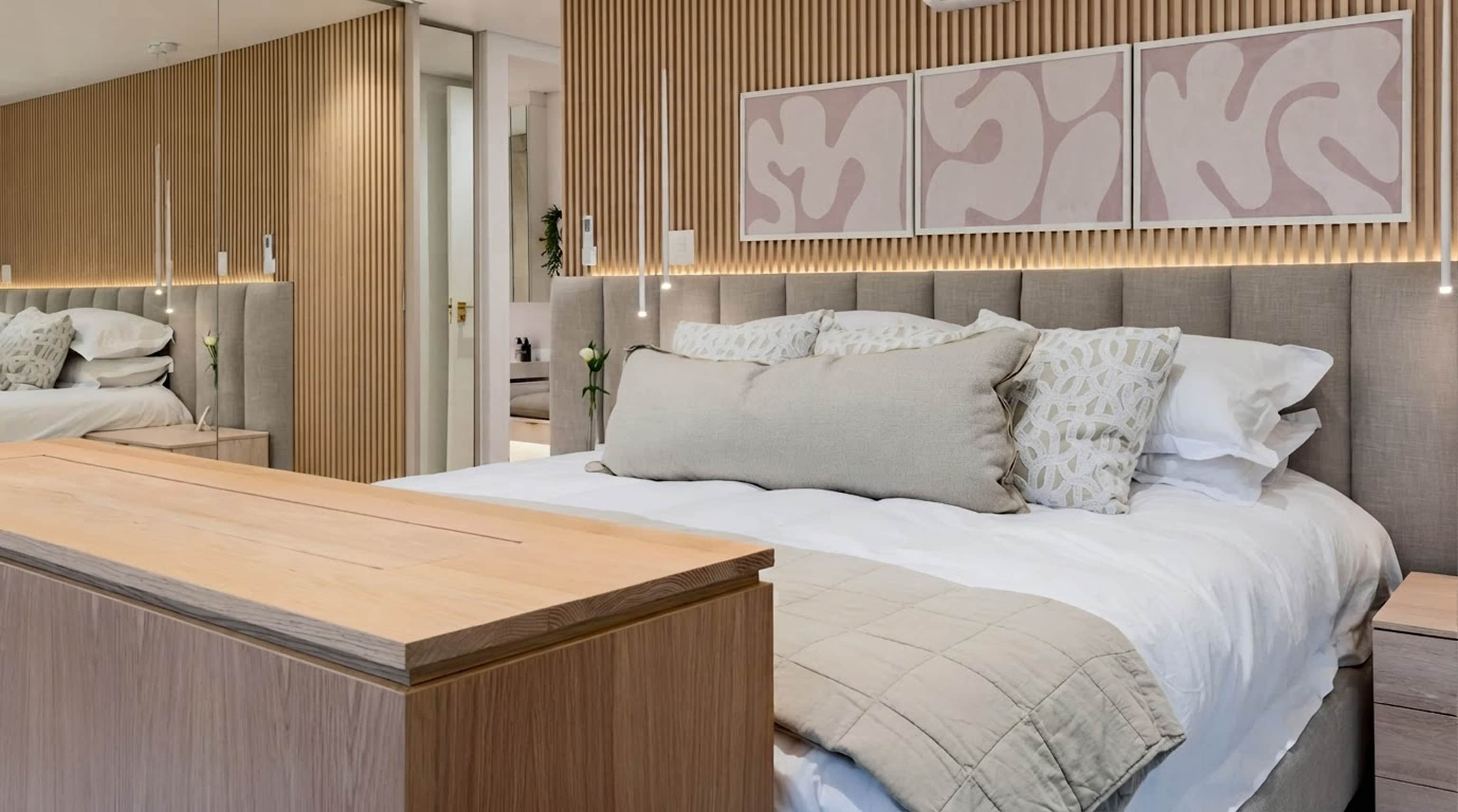 Bedroom with slatted oak wall panelling, an upholstered headboard and three framed abstract prints
