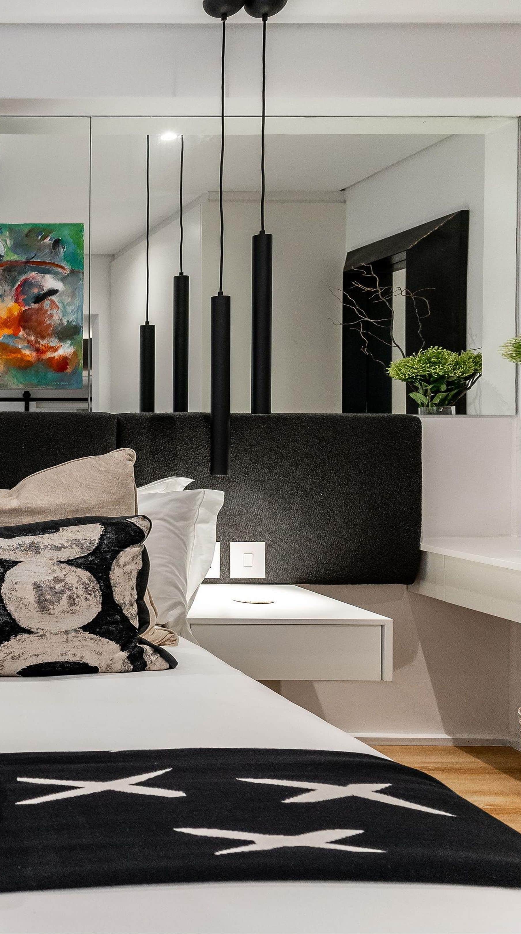 Bed with a black upholstered headboard, black pendant lights and a mirrored wall