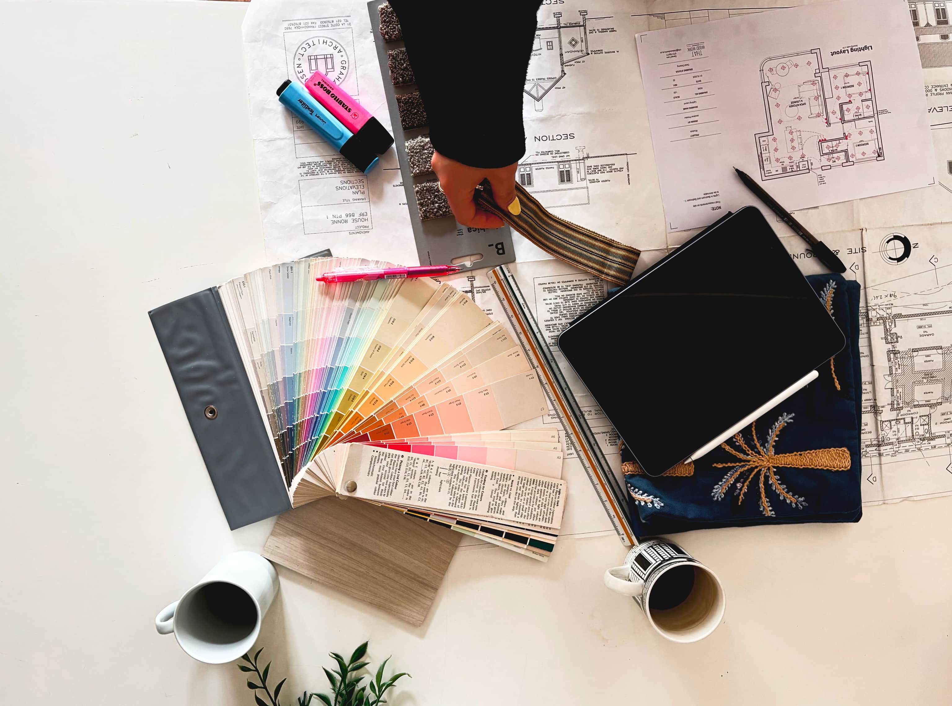 Designer’s desk with floor plans, a paint swatch fan, a notebook and coffee cups