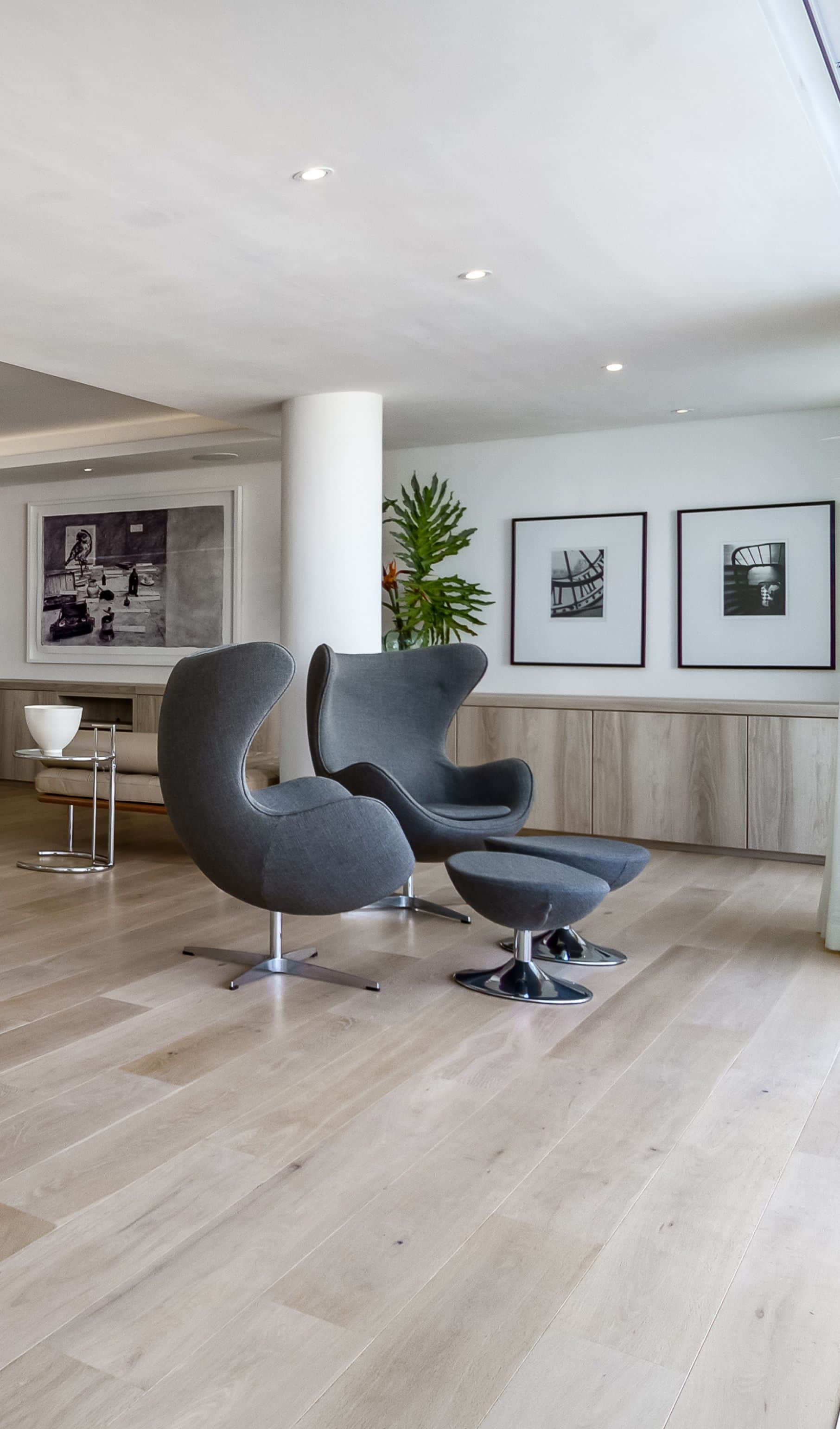 Pair of grey egg chairs with footstools on a pale oak floor beside framed black and white photographs