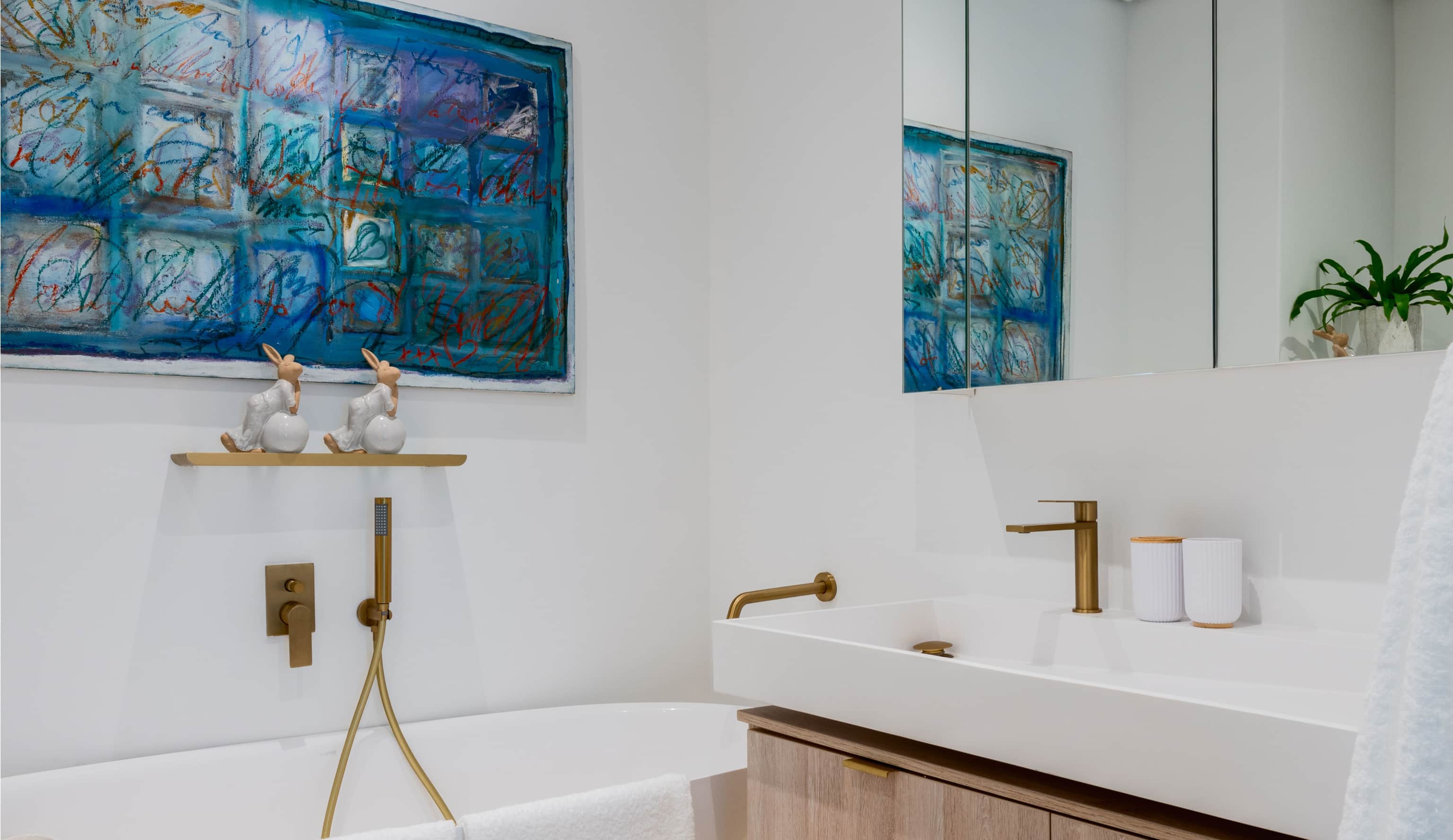 Bathroom with a freestanding bath, brass taps, an oak vanity and a blue mosaic artwork