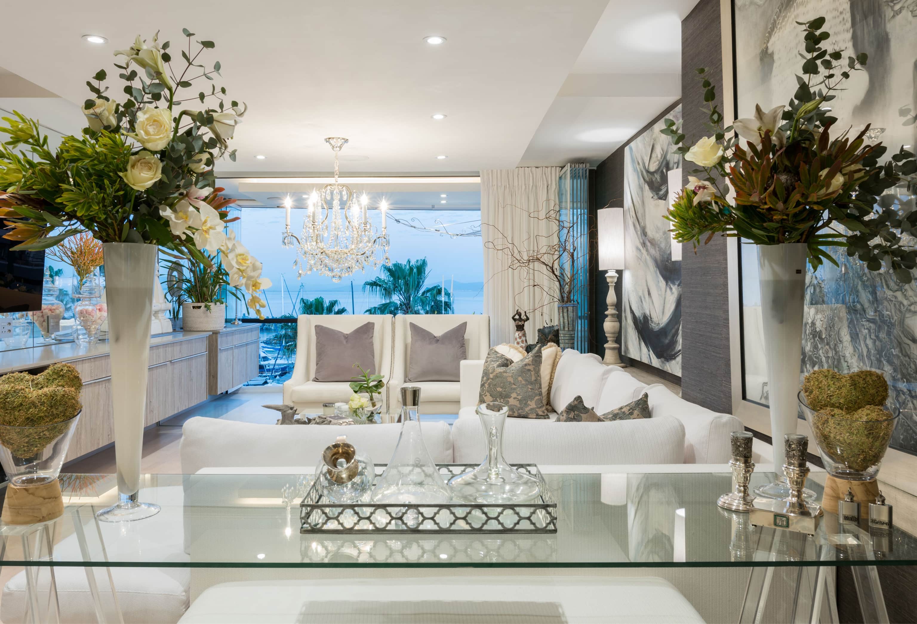 Lounge with white sofas and a crystal chandelier, seen across a glass table toward the marina