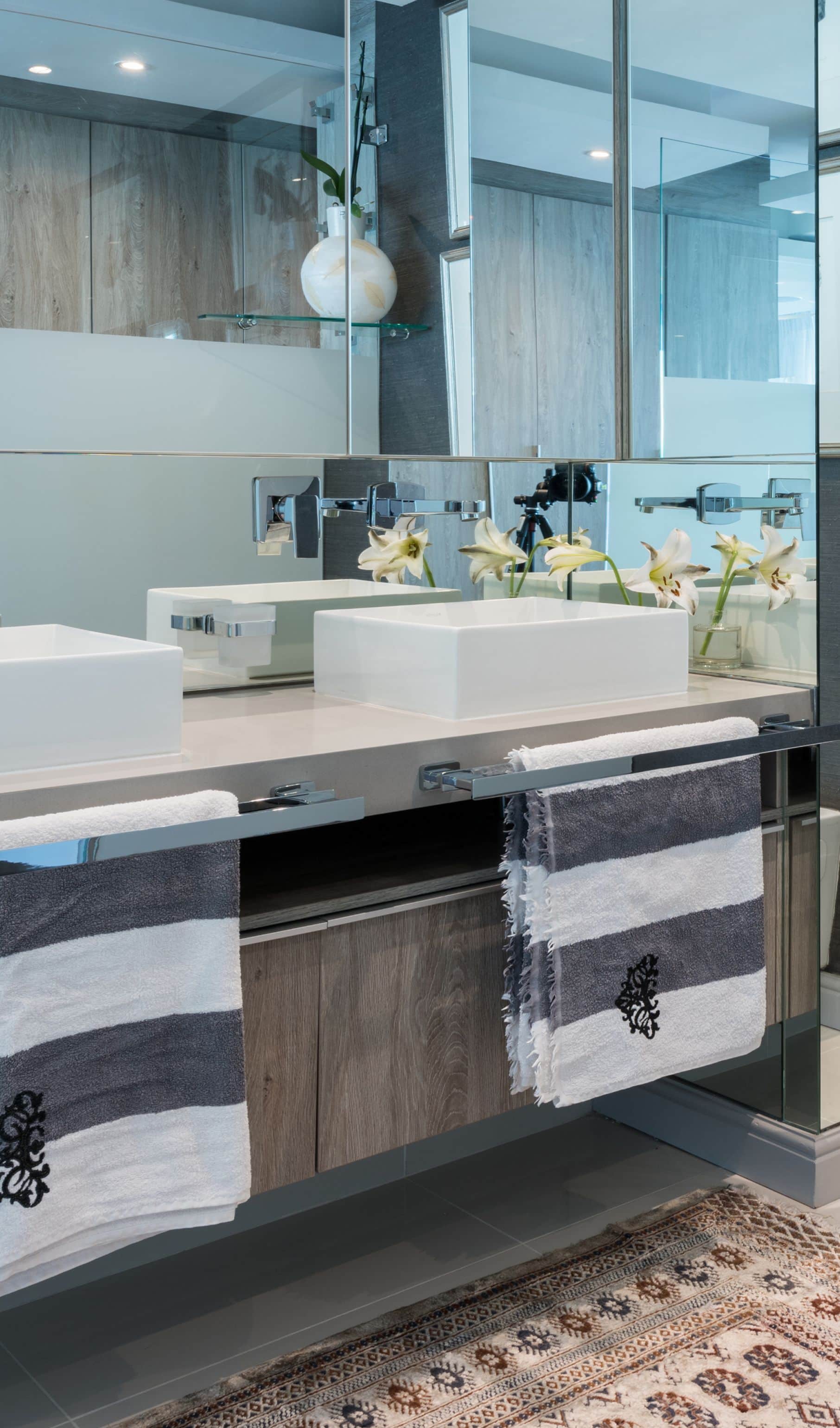 Twin white basins on a floating vanity with striped towels and white lilies