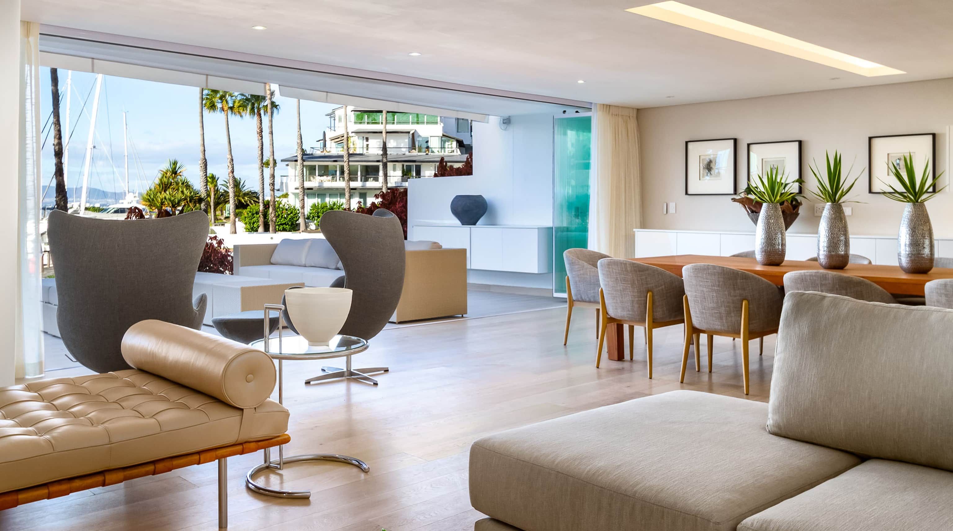 Open-plan living area with grey egg chairs, a tufted daybed and dining table, open to the Granger Bay marina
